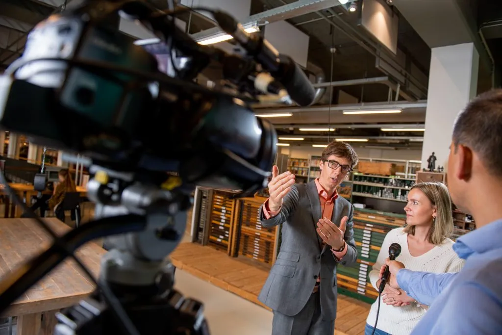 Een cameraploeg filmt een interview tussen de boekenkasten van een bibliotheek.
