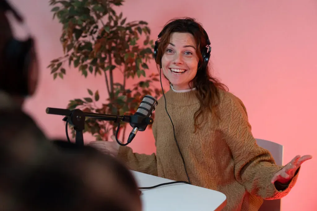 Een vrouw met koptelefoon praat in een microfoon tijdens een podcastopname.